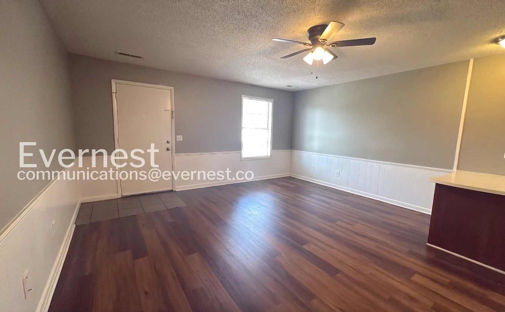 Unfurnished Midtown Manor living room with wood-look flooring, white wainscoting, and a ceiling fan